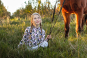 Young girl with braided hair sitting on the grass next to a horse