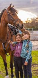 Two children standing next to a brown horse in an outdoor setting with trees and sky in the background.