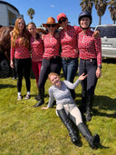 Group of equestrian riders posing outdoors with a horse in the background