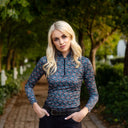 Woman in a patterned shirt standing outdoors with trees and a path in the background